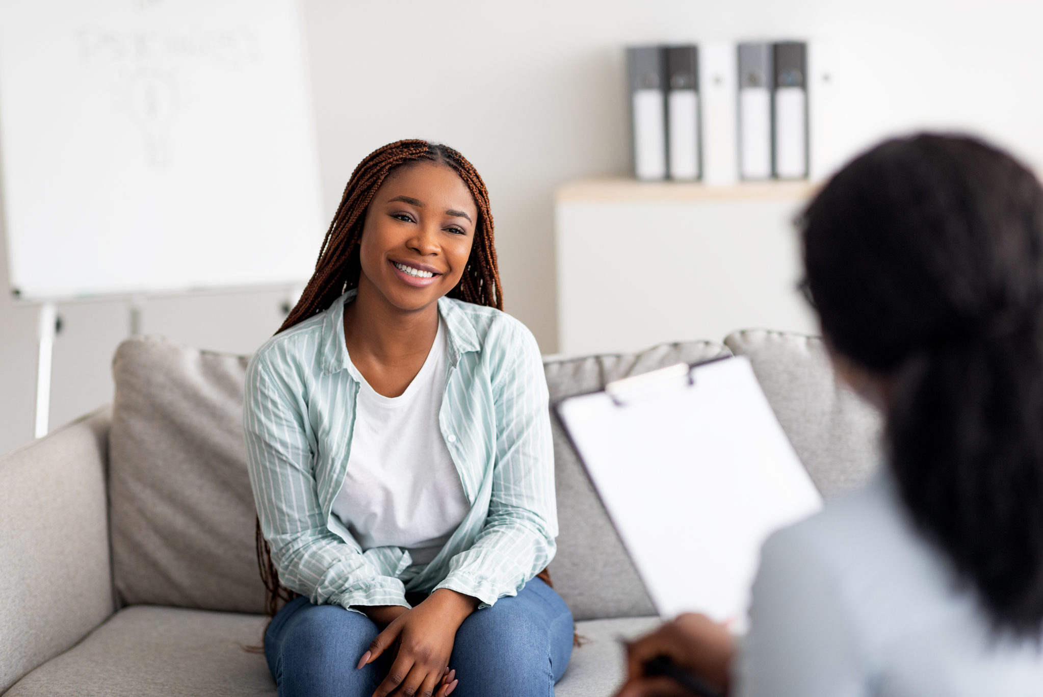 Successful therapy. Young female client having consultation with psychologist, grateful for professional help at clinic. Happy black lady speaking with her psychotherapist, solving emotional problem